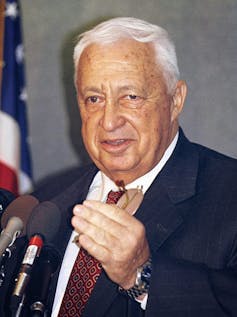 Ariel Sharon speaking into microphones.