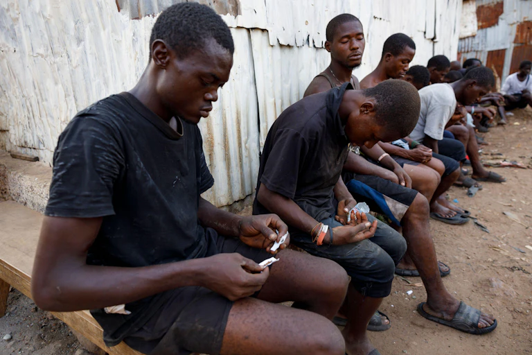 A group of young men gather, some are preparing drugs, others are sleeping.