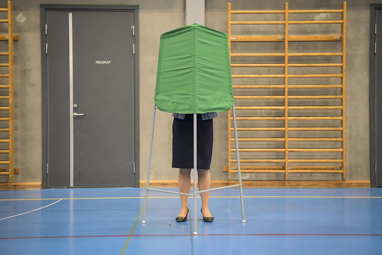 A woman's bottom half visible as she casts a vote in a voting booth. Her top half is behind a fabric privacy shield.