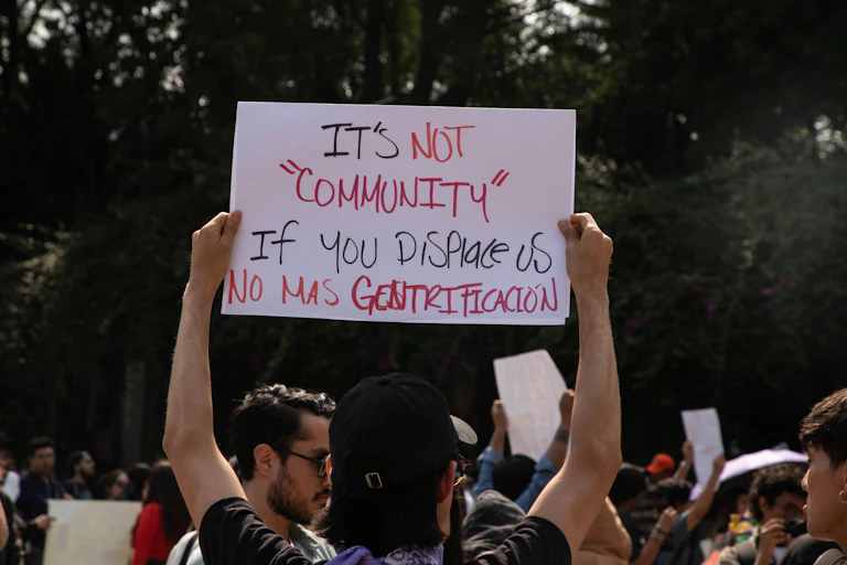 A Mexican protester holds a sign reading 'it's not community if you displace us'.