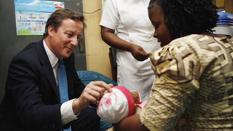 A white man in a suit and tie beholds a baby held by a Black woman in a clinic.