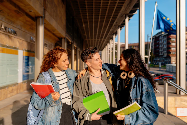 Three university students walking and chatting outdoors, an EU flag is seen in the background