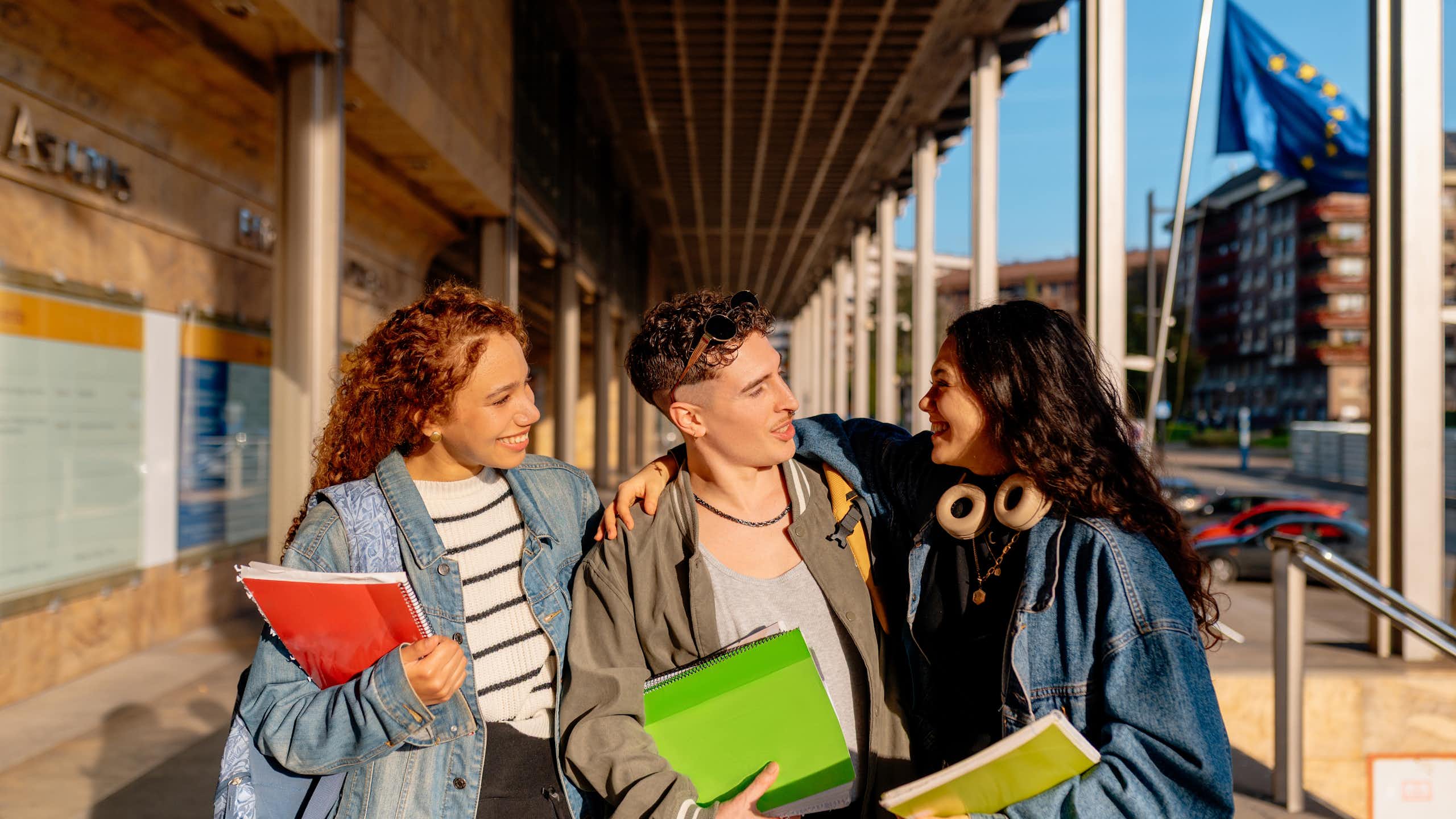Three university students walking and chatting outdoors, an EU flag is seen in the background