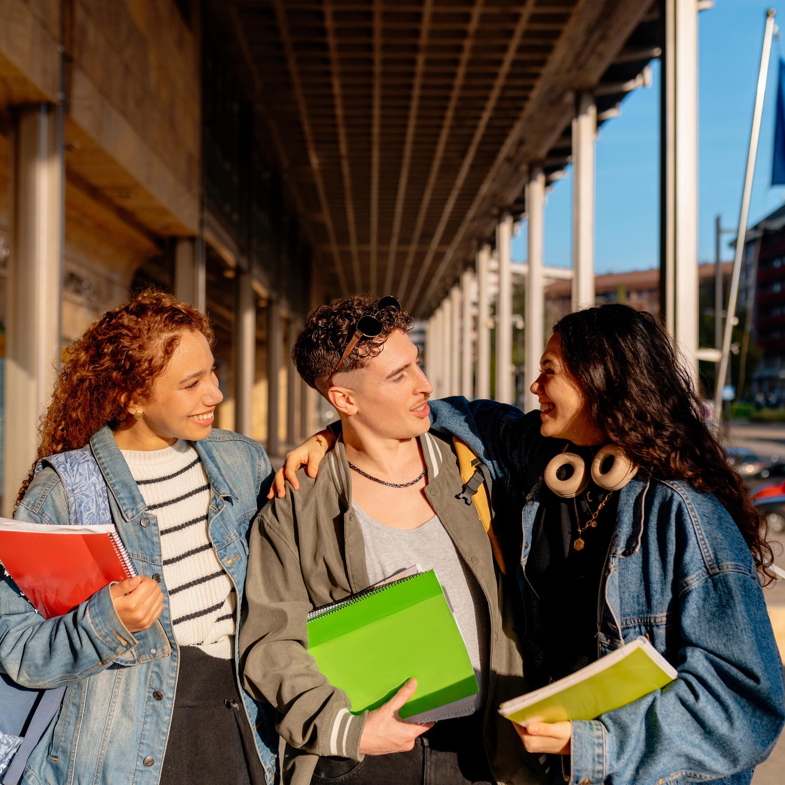 Three university students walking and chatting outdoors, an EU flag is seen in the background