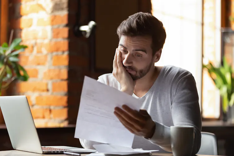 A young man looks dejectedly at a bill