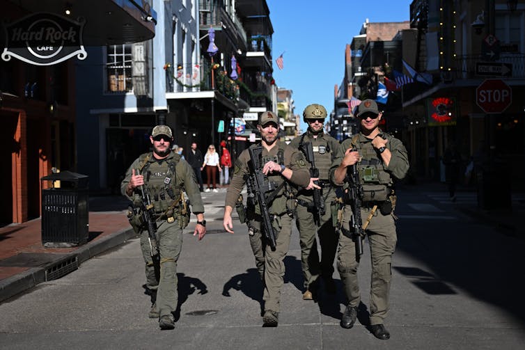 Four men dressed in military gear walk along a city street.