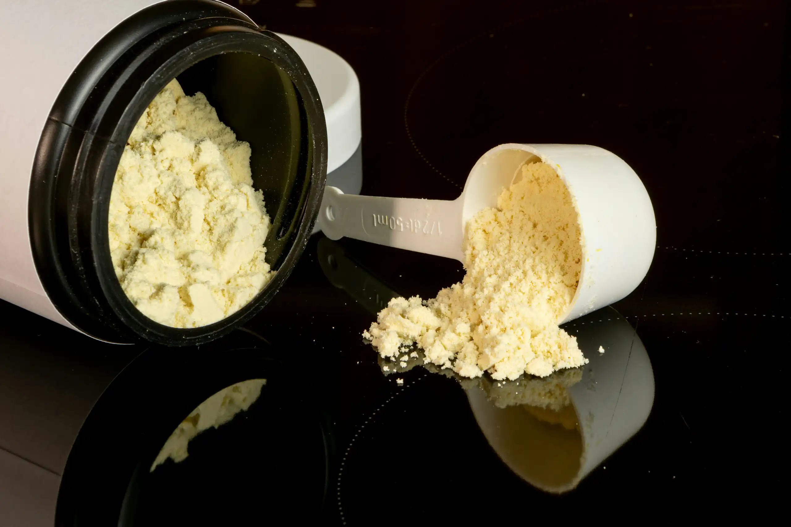 A jar of powdered supplement on its side and a scoop with a small pile of powder