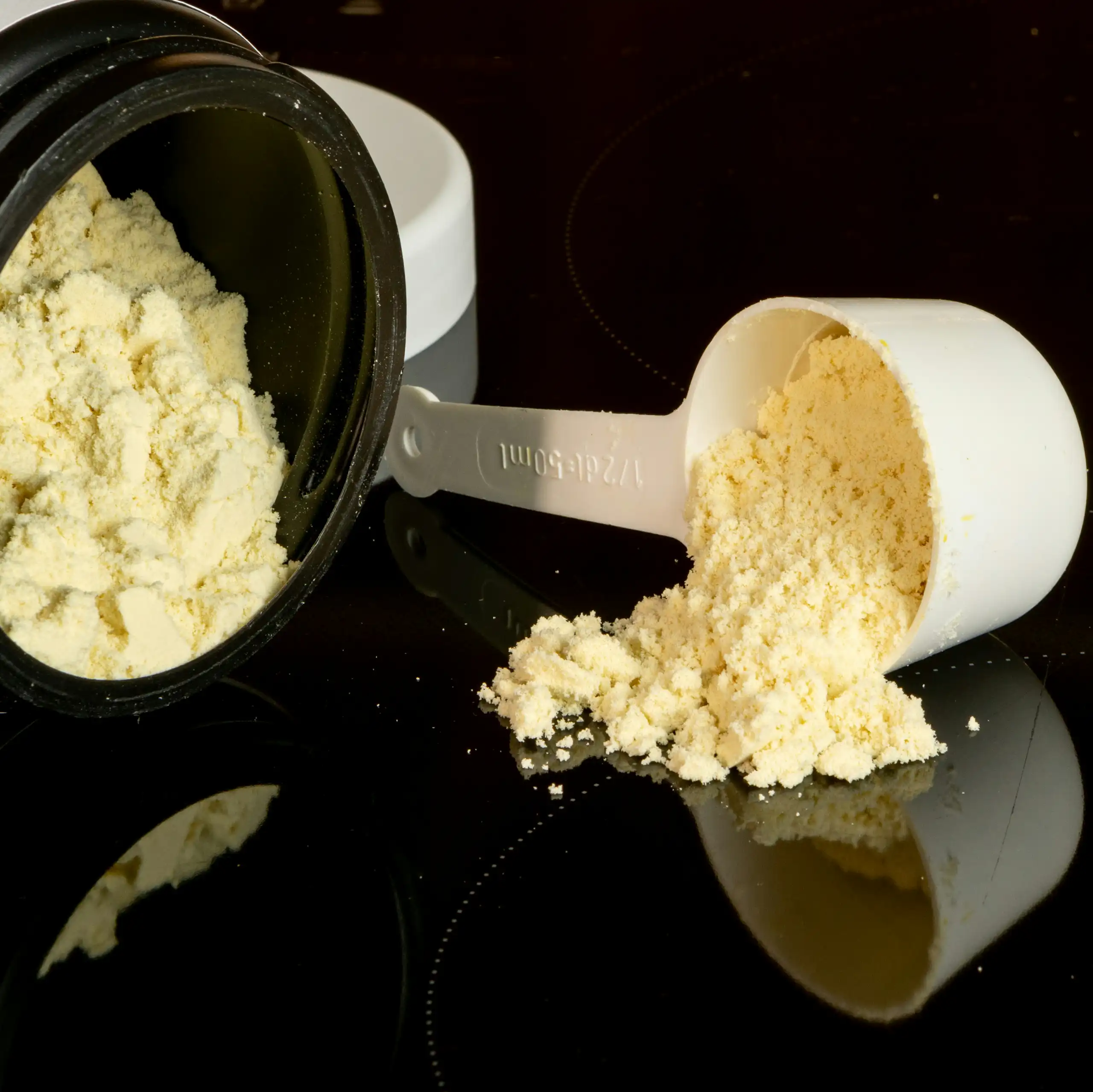 A jar of powdered supplement on its side and a scoop with a small pile of powder