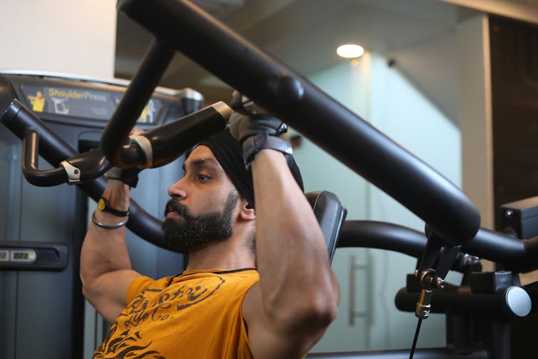 Hombre barbudo con una camiseta amarilla con una máquina de pesas en el gimnasio