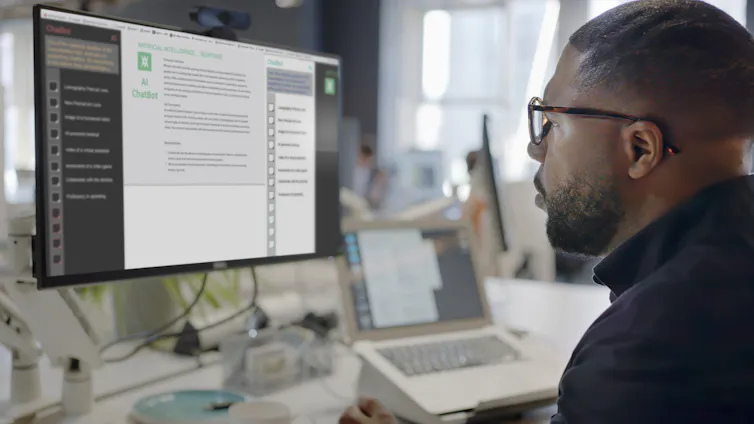 a Black man wearing glasses looks at a computer screen in an office