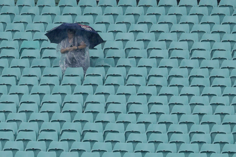 A woman in raincoat and umbrella sits in empty stadium seats