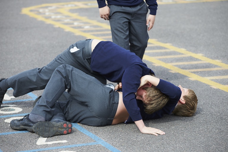 Two boys wrestle (or fight) in a school playground.