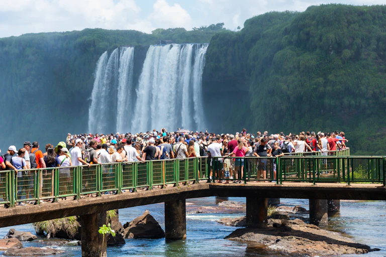 A crowded viewing platform with waterfalls in background.