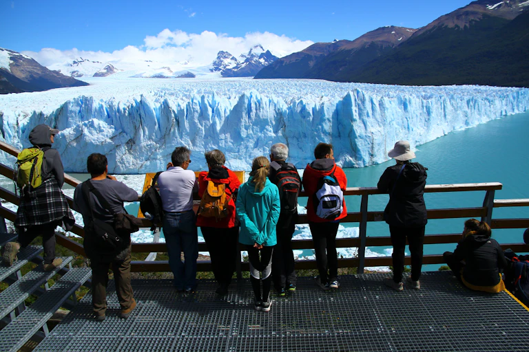 People on wooden platform look at large glacier front