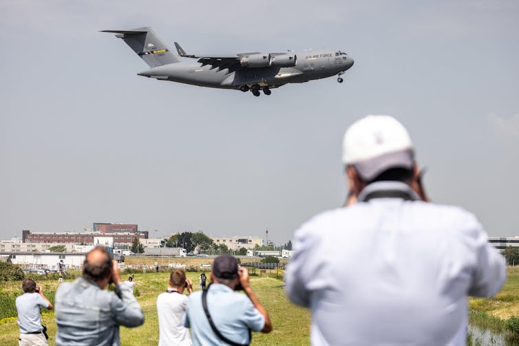 People taking pictures of a US Air Force transport plane as it takes off.