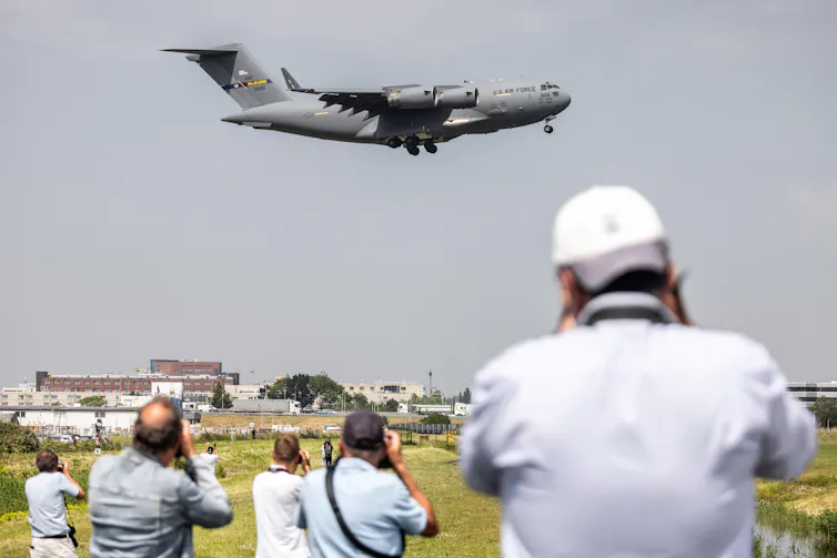 People taking pictures of a US Air Force transport plane as it takes off.