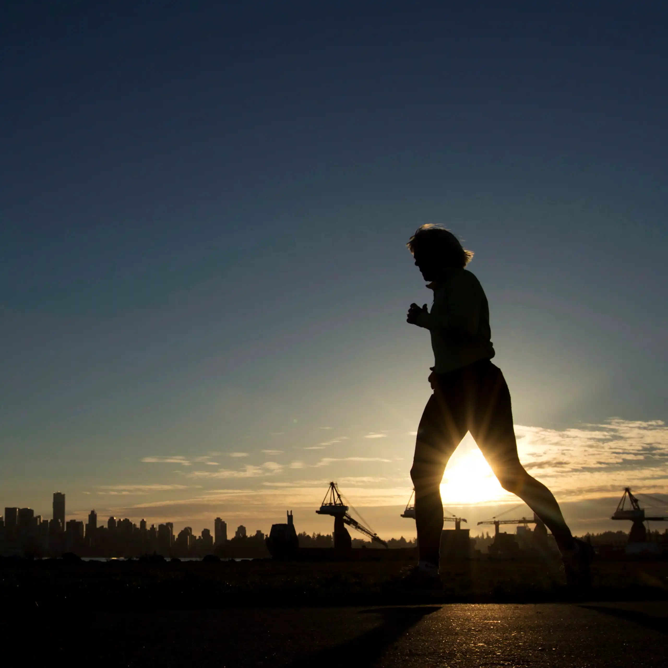 A woman is silhouetted as she runs along the water front in North Vancouver, B.C.