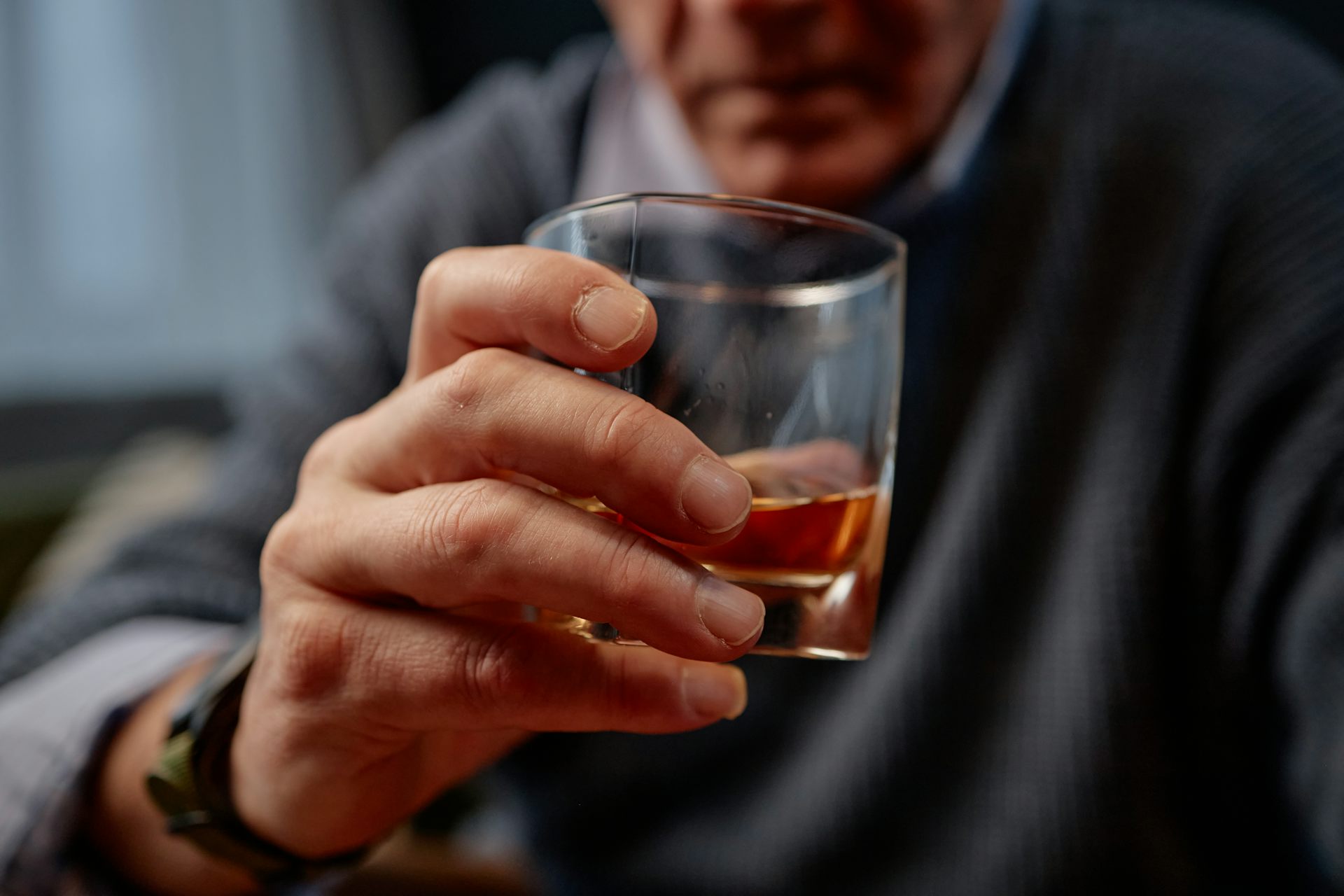 Gros plan sur la main d’un homme d’un certain âge tenant un verre qui semble contenir de l’alcool.
