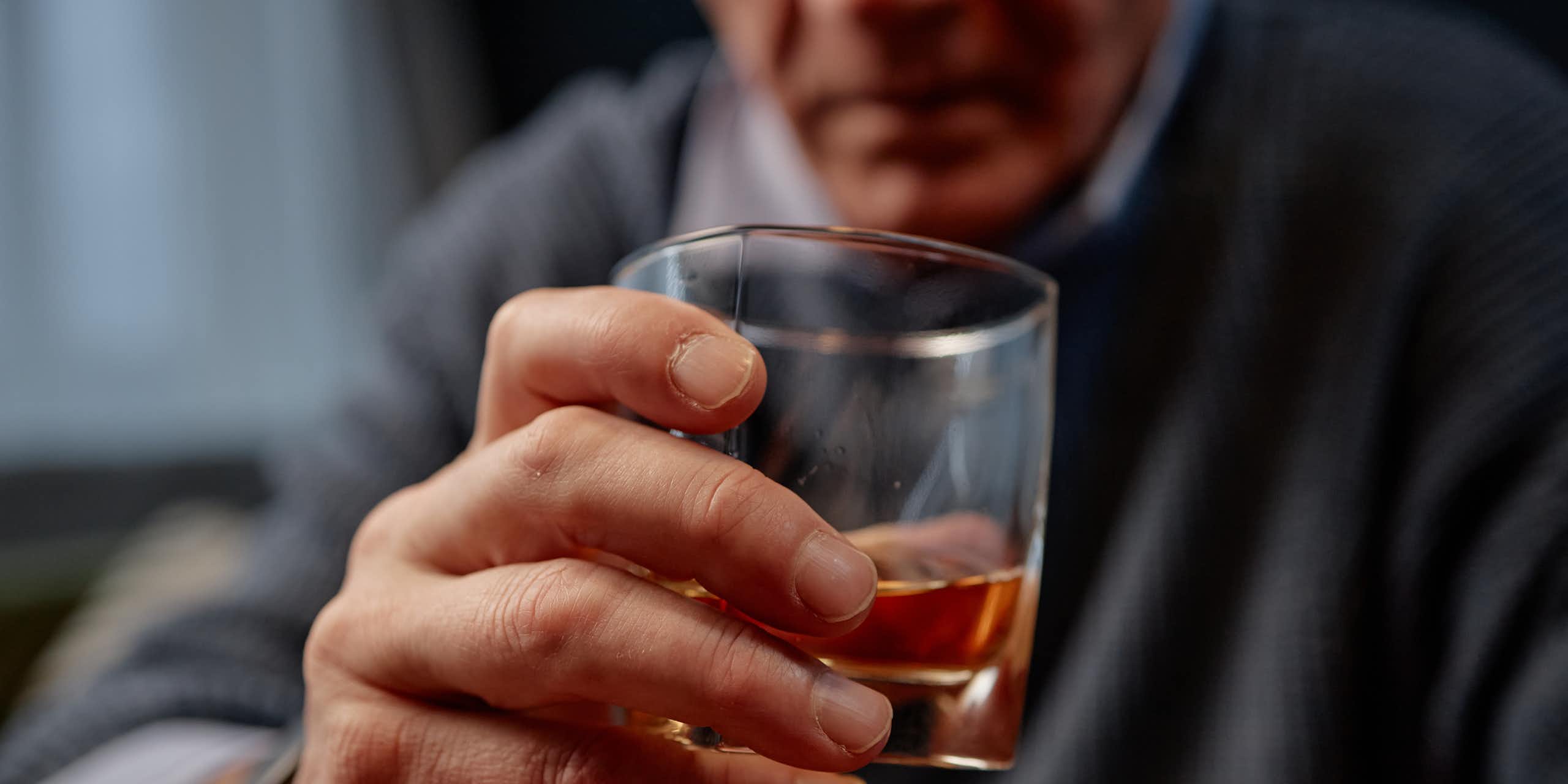 Gros plan sur la main d’un homme d’un certain âge tenant un verre qui semble contenir de l’alcool.