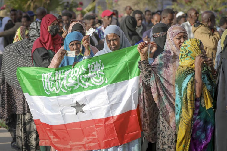 Canadá y el reconocimiento condicional de Palestina en el Reino Unido revelan reglas desiguales de la condición de estado 2 Un grupo de mujeres en hijabi contiene una bandera de rayas verde, blanca y roja que tiene una estrella negra en el medio y Shahad en un escenario caligráfico blanco