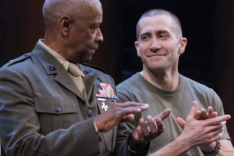 Two men in military clothing clapping on a stage.
