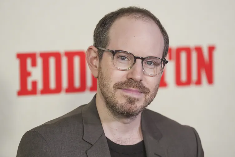 A white man in a blazer and glasses stands in front of a backdrop that says 'Eddington'