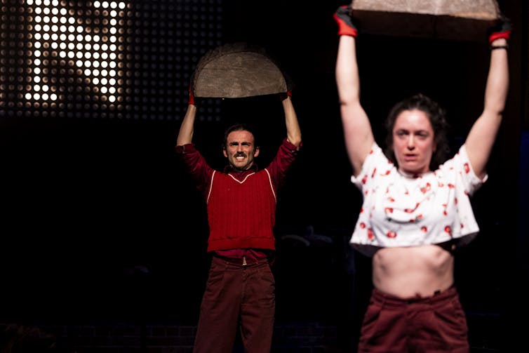Actors hold up large blocks of wood or tree stumps.