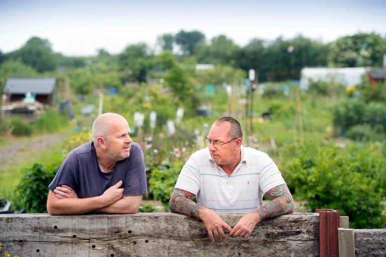 two men lean on a fence