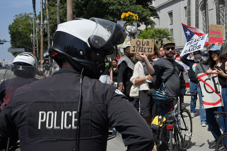 In foreground police office with helmet and protesters.