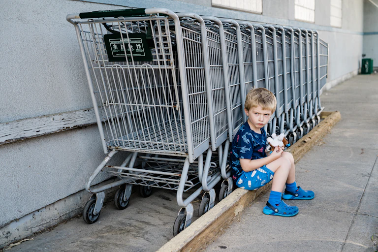 A little boy pouts next to a row of shopping carts.