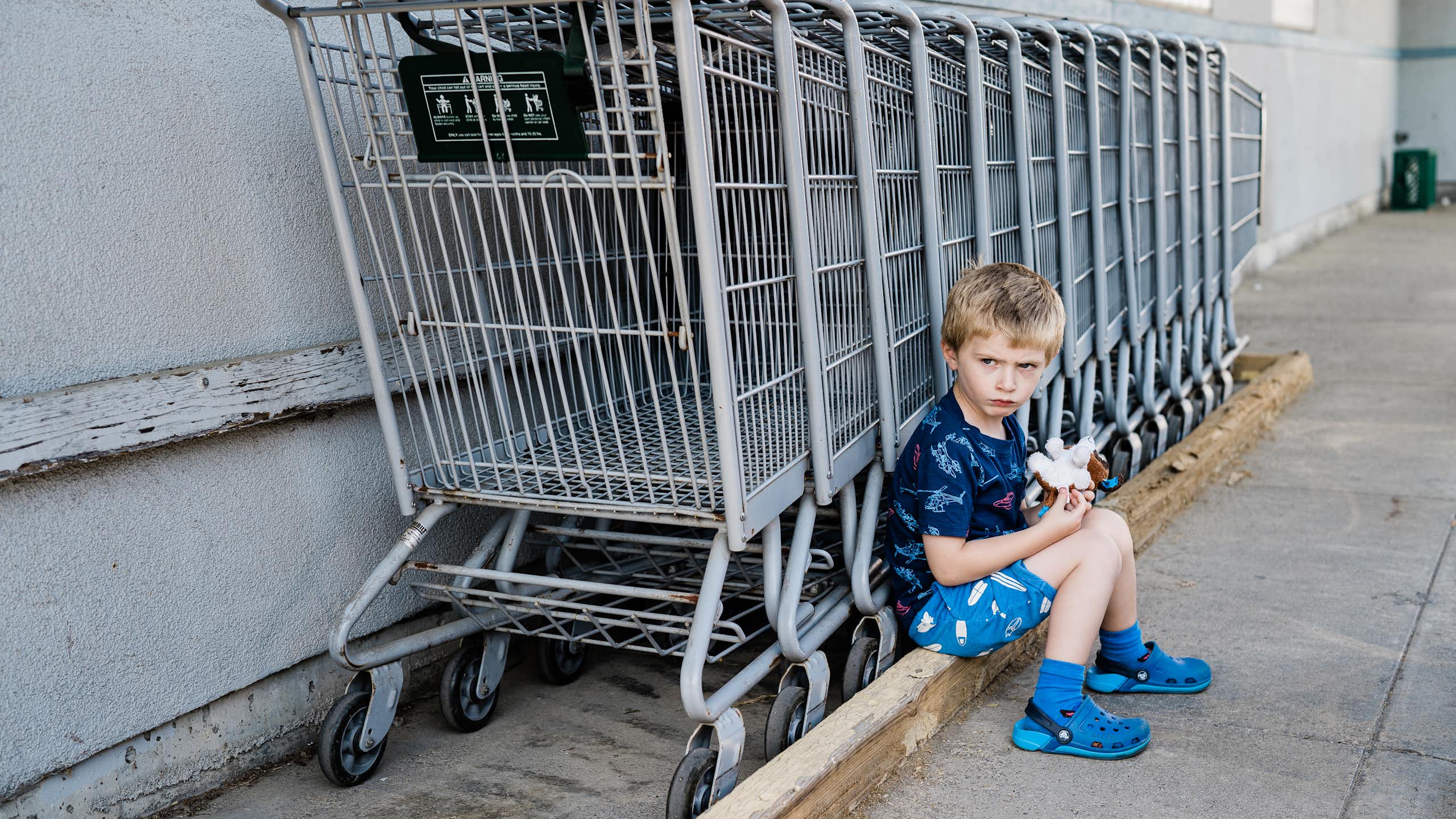 A little boy pouts next to a row of shopping carts.