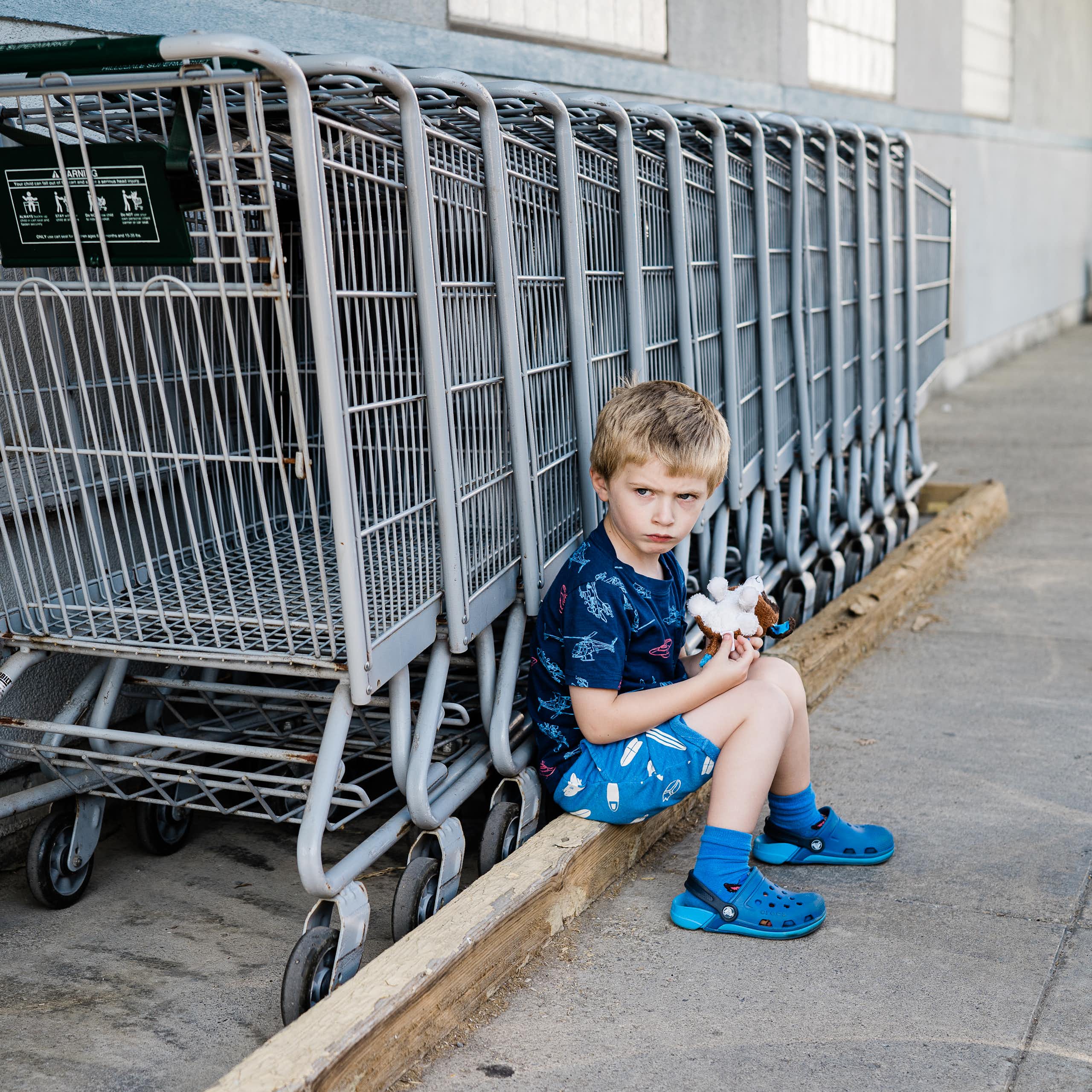 A little boy pouts next to a row of shopping carts.