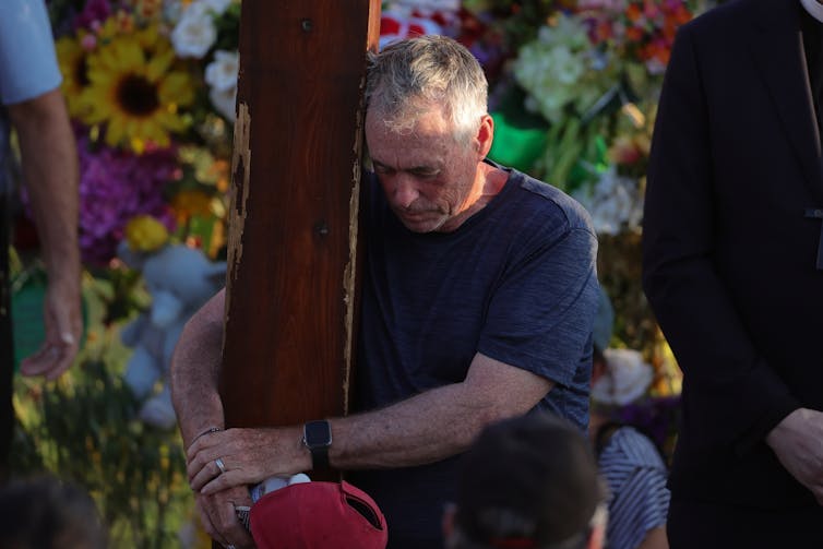 A man clutches a tree post in mourning.
