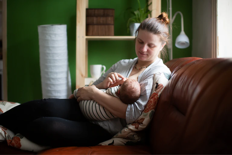 A woman sitting on a couch breastfeeding her baby.