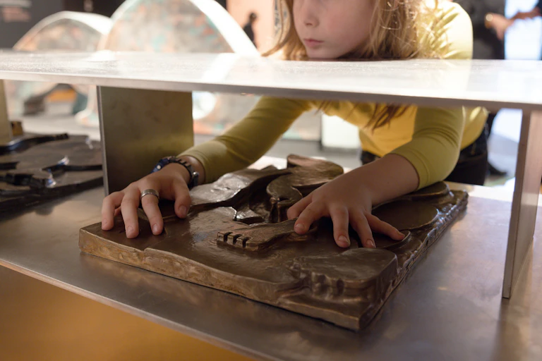 A young child feels a bronze relief.