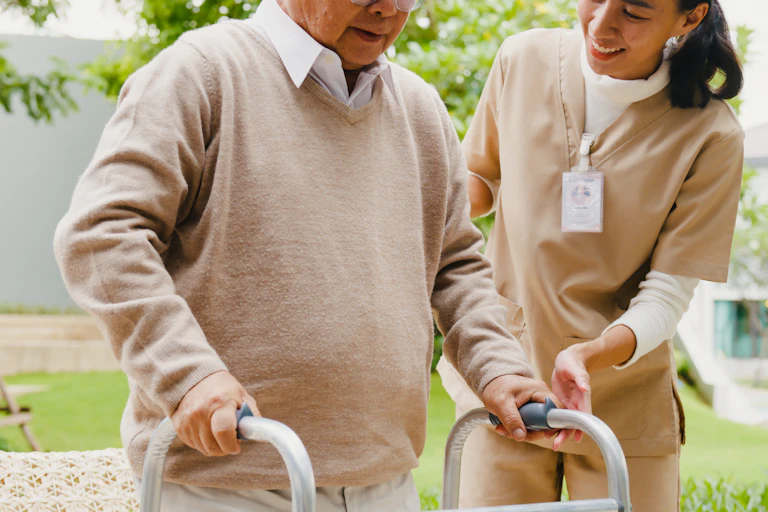 A caregiver helps an older man to walk with a walker.