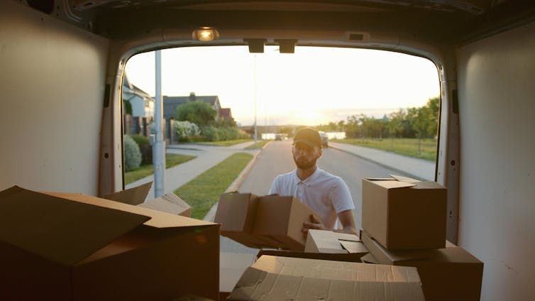 A man unloads moving boxes from the back of a van.