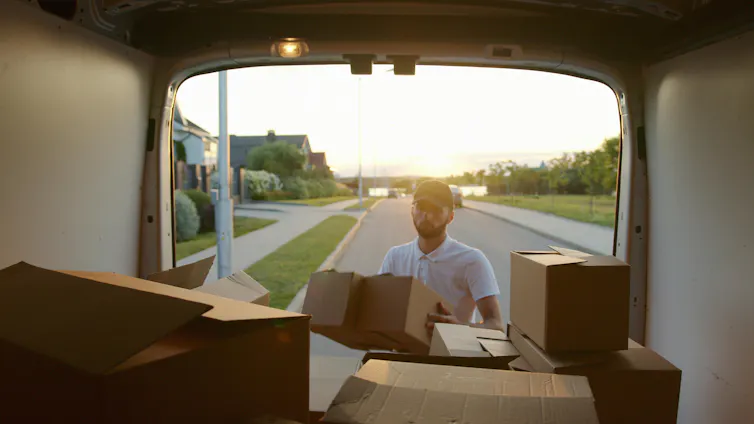 A man unloads moving boxes from the back of a van.