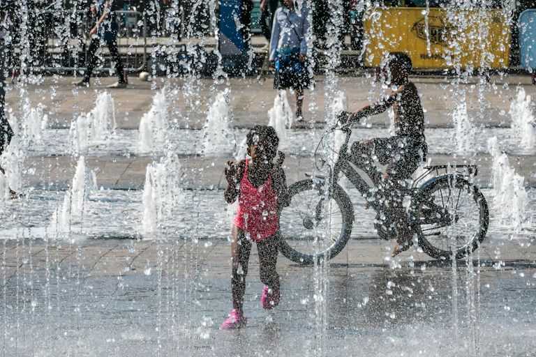 girl in swimsuit and boy on bike in water fountains in London