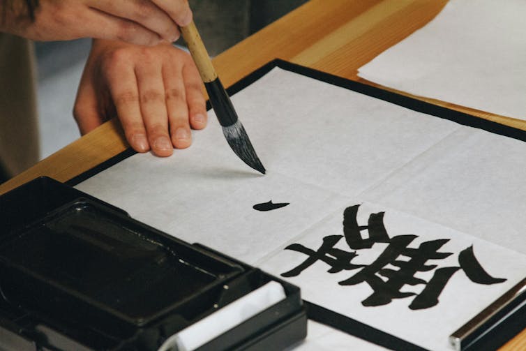 Hand holding a brush and writing a Chinese character
