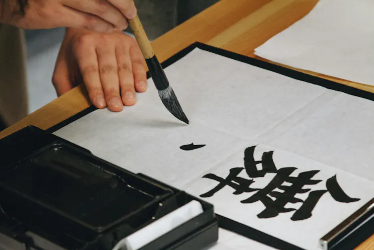 Hand holding a brush and writing a Chinese character