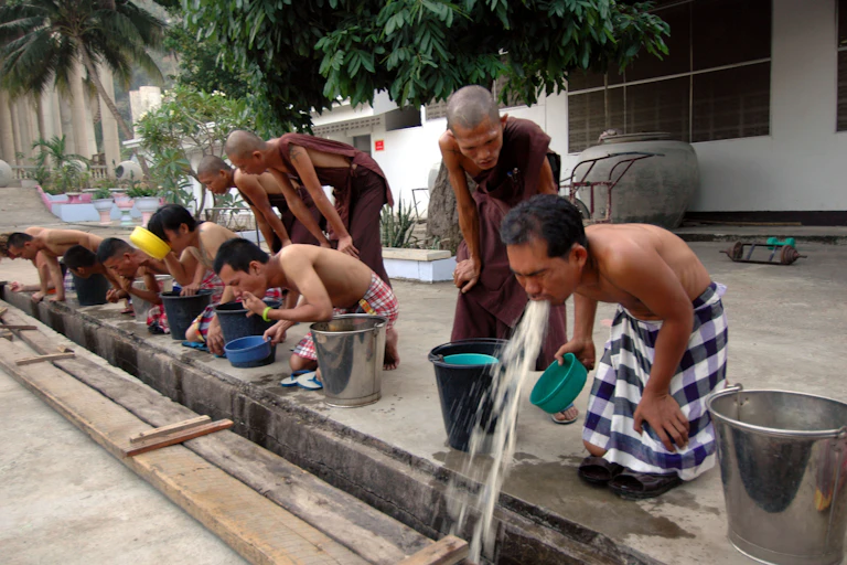 A row of men vomitting while Buddhist monks look on.