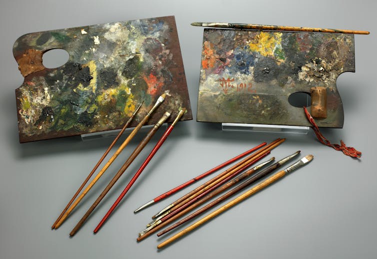 two boards with various colors of paint dried on them along with multiple paint brushes