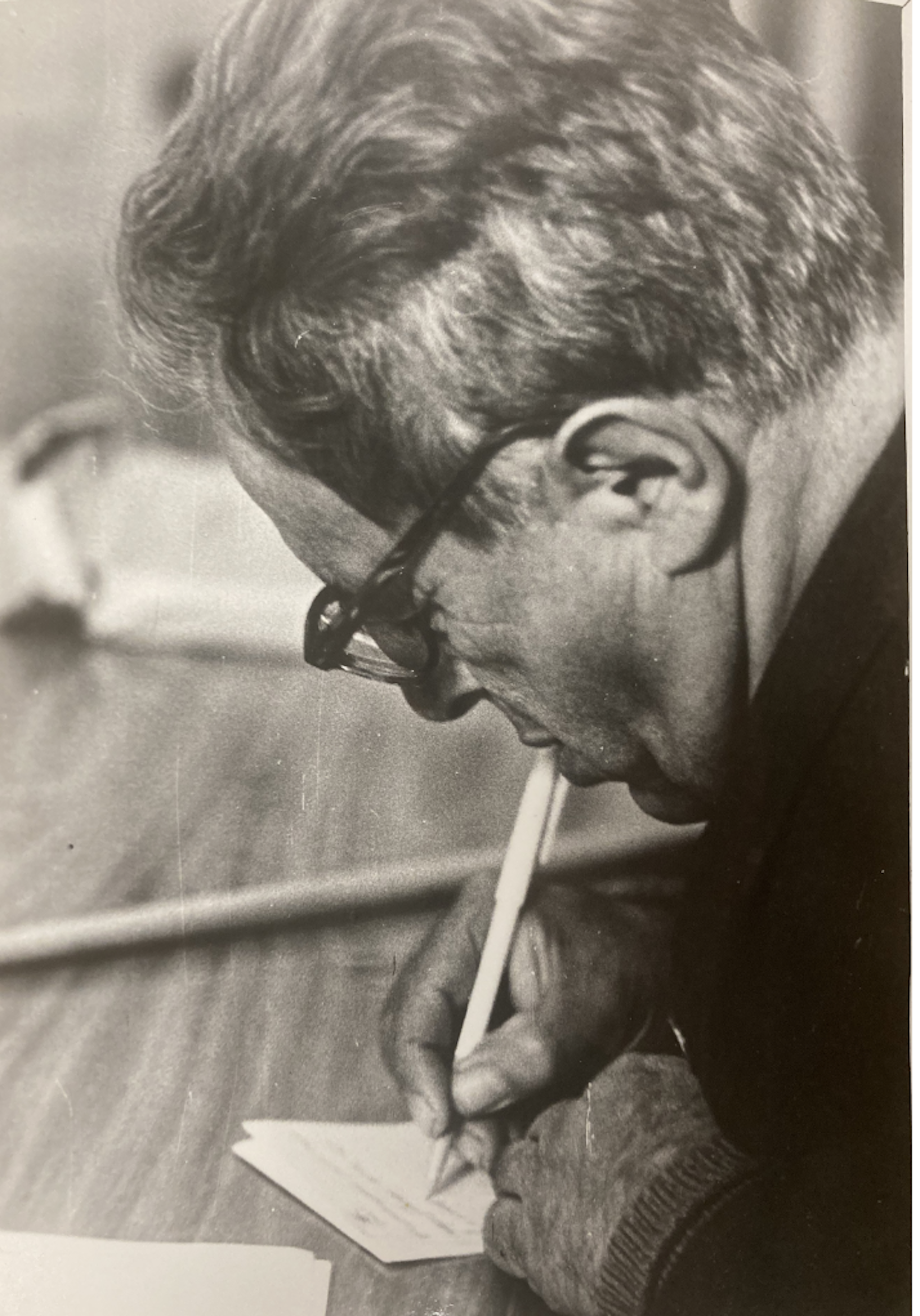 A man sitting at a desk, writing with a pen.