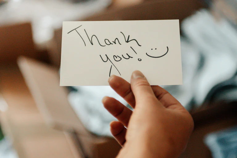 a hand holding a handwritten thank you note