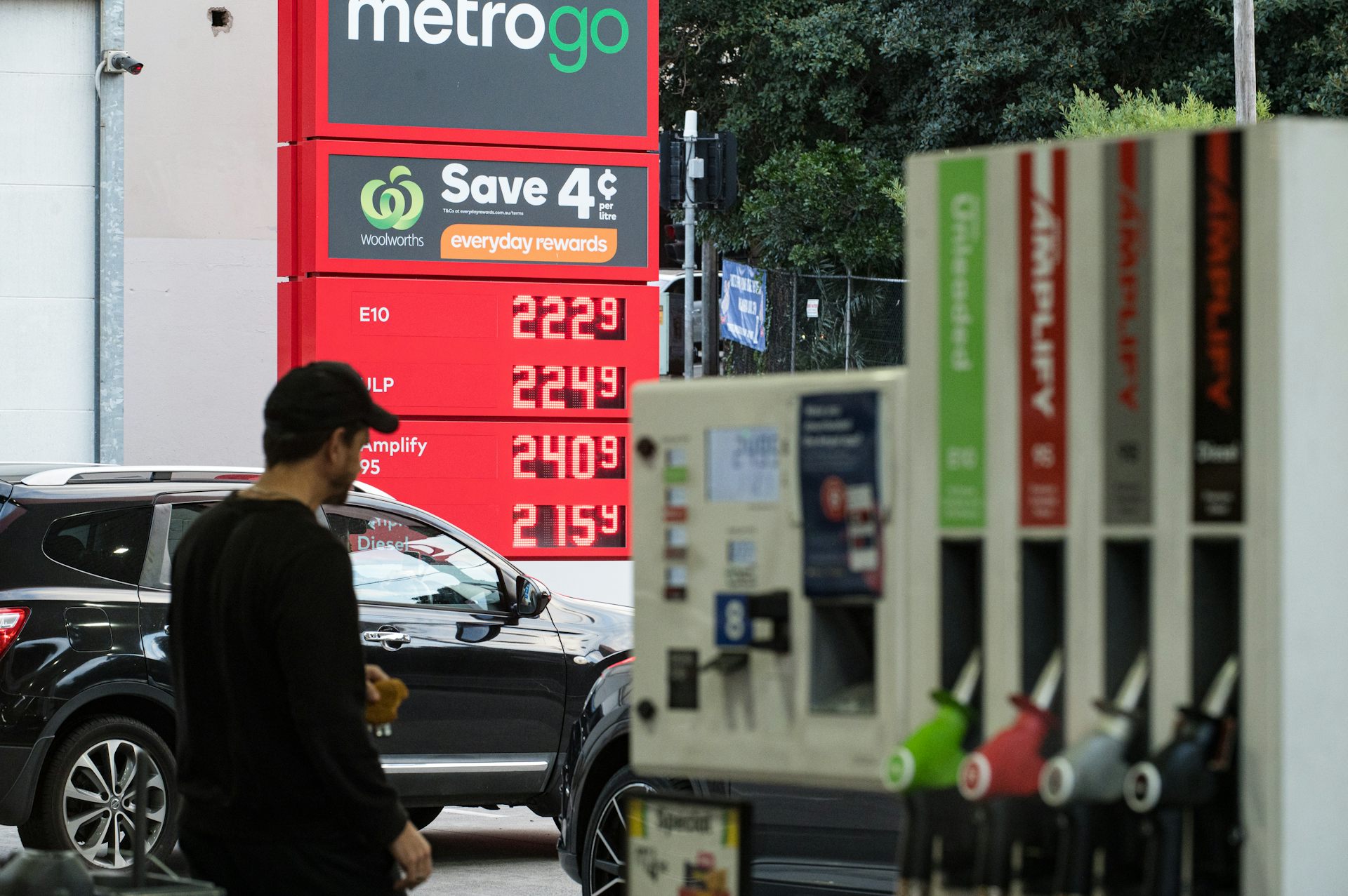 A man in a black cap and top walks through petrol station.