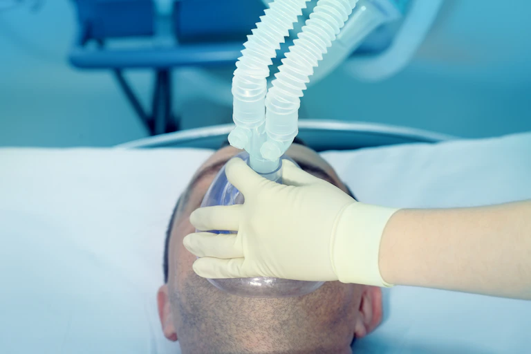 Una mano enguantada sostiene una mascarilla con tubos.