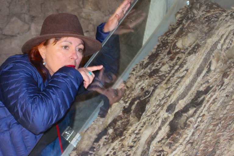 A woman in a hat pointing at an intricate weaving.