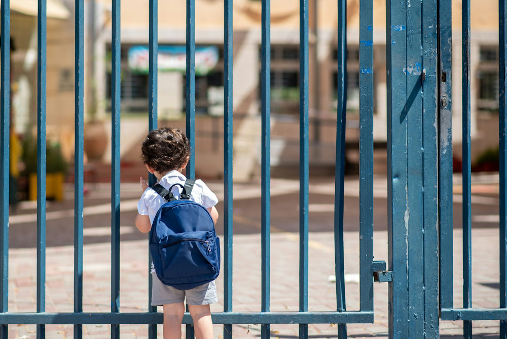 Young child with backpack stands at closed metal gates