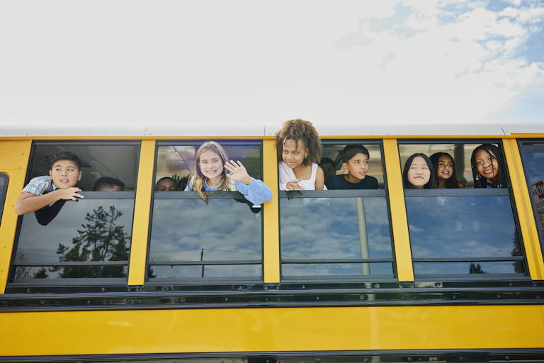 Children stick their heads out of a stopped yellow school bus and waving.